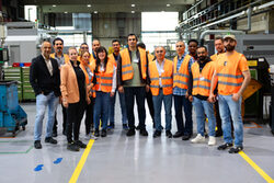 Die Teilnehmende Gruppe mit Mitarbeiter/innen von Stahlwille und von der Servicestelle Arbeits- und Fachkräfte stehen Mitte der Produktionshalle mit Orangen Sicherheitswesten