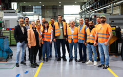 Die Teilnehmende Gruppe mit Mitarbeiter/innen von Stahlwille und von der Servicestelle Arbeits- und Fachkräfte stehen Mitte der Produktionshalle mit Orangen Sicherheitswesten