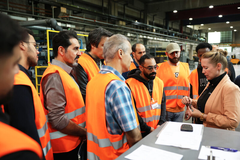 Teilnehmenden mit orangen Sicherheitswesten schauen sich ein Objekt an einem Tisch