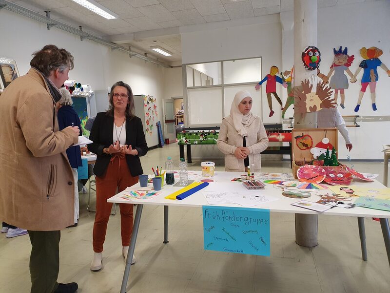 3 Personen stehen an einem Tisch mit Infomaterial zu den Arbeiten der Frühfördergruppe