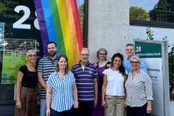 Mitarbeitende des Ressorts Zuwanderung stehen vor einer Regenbogenfahne am Eingang des Hauses der Integration